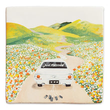 Afbeelding in Gallery-weergave laden, StoryTile - Just married. Net getrouwd! Deze StoryTile toont een witte auto met op de achterruit de woorden &#39;Just married&#39;. Achter de auto hangen lege blikjes. De auto rijdt door een heuvellandschap met bloemen in het veld.  
